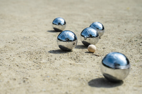 Steel petanque balls in mix of sunlight and shade on gravel court, chrome reflections and soft shadows on playing surface