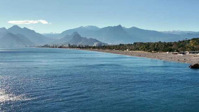Wide panoramic view of Konyaalti beach in Antalya with calm Mediterranean sea and majestic taurus mountains range.