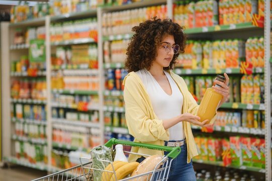 Customer choosing juice in supermarket with shopping cart