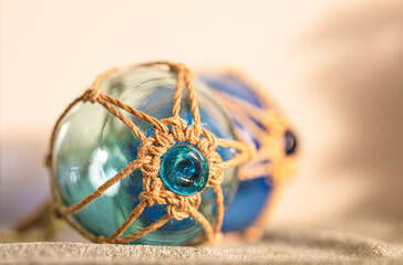 Close up of blue glass fishing float with rope net decoration on wooden surface in soft natural light. © Trygve