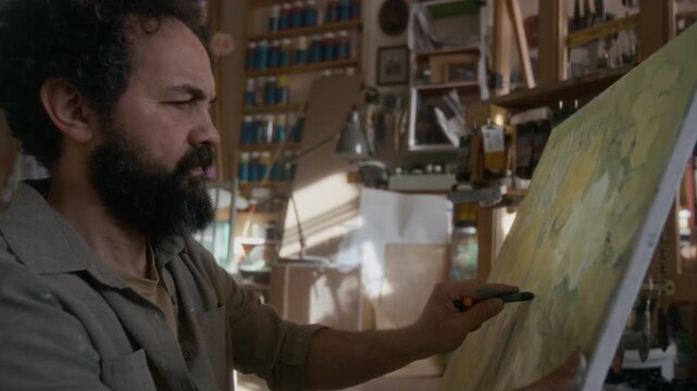 Stressed male painter drawing impulsively with graphite stick, throwing away canvas in despair, then trying to finish his artwork