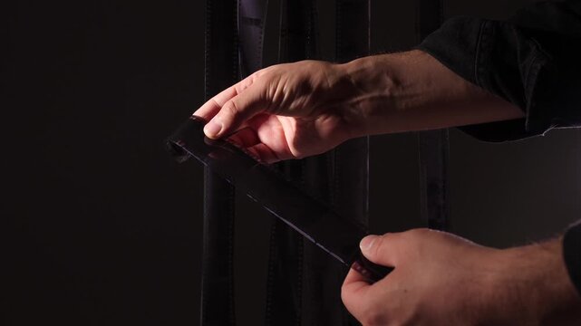 Hands examining a strip of developed black and white film negative showing individual frames, symbolizing the analog process of photography and film development
