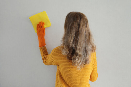 House cleaning, woman in rubber protective gloves with rag wiping the surface of wall