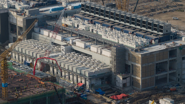 Aerial view of the Bridge Data Center under construction with cooling units, industrial cranes, and workers on site in Khlong Tamru, Chon Buri, Thailand.