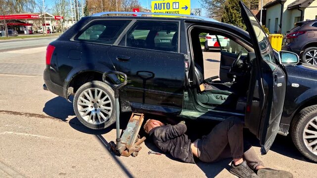 Mechanic working under lifted car in outdoor auto repair area on a sunny day
