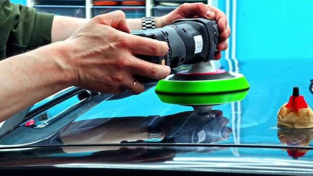 Car polishing with electric buffer and green pad on glossy vehicle surface