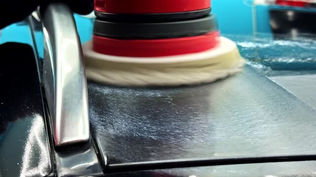 Close-up of a rotary polisher buffing a black car panel, showing paint correction, gloss enhancement, and professional auto detailing in action.