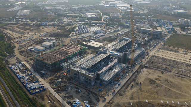 Aerial view of the Bridge Data Center construction site with cranes and industrial buildings under a clear sky in Khlong Tamru, Chon Buri, Thailand.