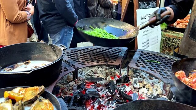 Delicious seafood, including prawns and scallops, sizzling in woks over a charcoal fire pit