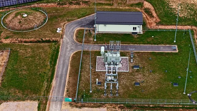 Aerial view of large solar farm featuring rows of photovoltaic panels, electrical substation, transformer, and control building generating renewable energy in Latvia
