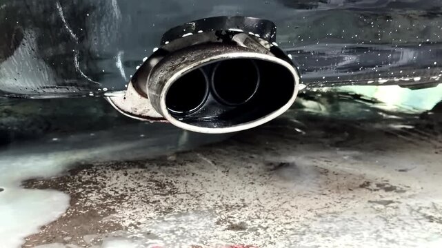Close-up Of Dual-tip Chrome Exhaust Pipe Of Black Vehicle Dripping Wet At Detailing Bay.