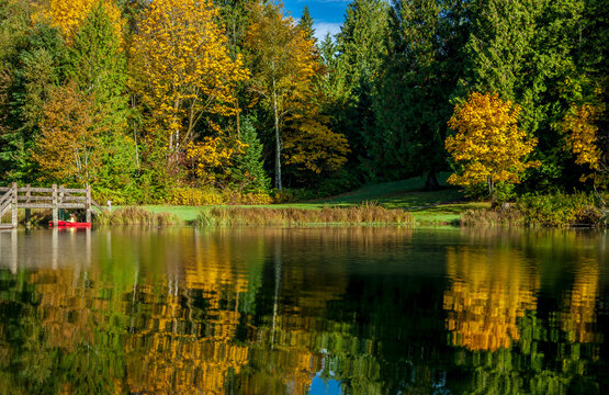 A woman paddles a red canoe on a calm still lake in autumn in northern Washington State