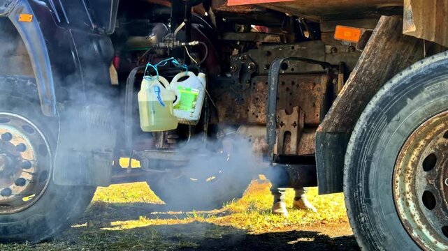 Close-up under a truck chassis with smoke or exhaust drifting around the wheels and mechanical components, capturing heavy vehicle operation and industrial transport detail.