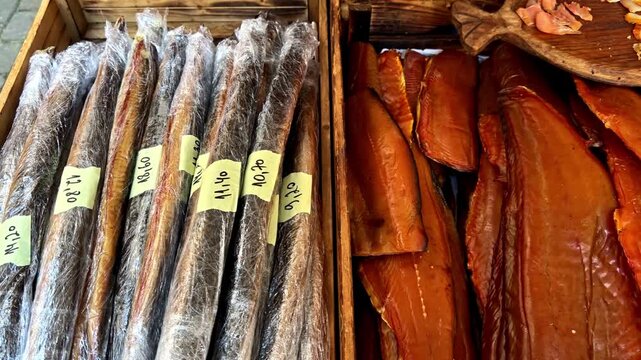 Wooden market crates filled with smoked fish fillets and long vacuum-wrapped fish, showcasing artisanal seafood products at an outdoor food stall.