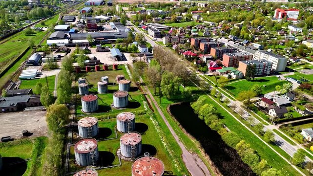 Aerial parallax over Soviet-era cylindrical fuel storage tanks separated by canal from residential neighborhood with railway in Jelgava, Latvia