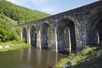 Fototapeta premium stone bridge with arches over a mountain river. forest on the hills.