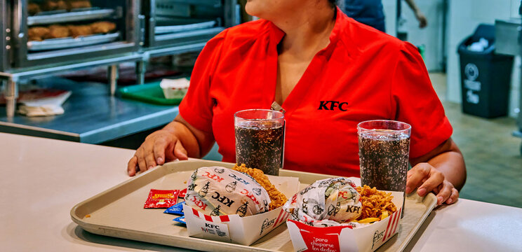 Ambato, Ecuador - June 09, 2025: KFC employee in red uniform serving delicious fast food meal at Mall de los Andes, showcasing vibrant atmosphere and customer service experience