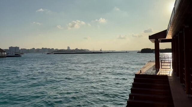 Wooden pier deck beside ocean with boats and distant shoreline under soft light Maldives