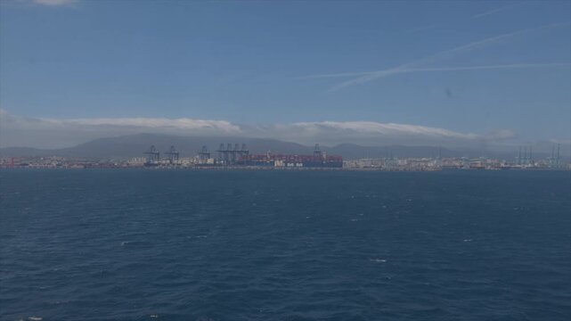 Distant view of Algeciras industrial port with cranes and container terminals across calm Mediterranean sea in southern Spain