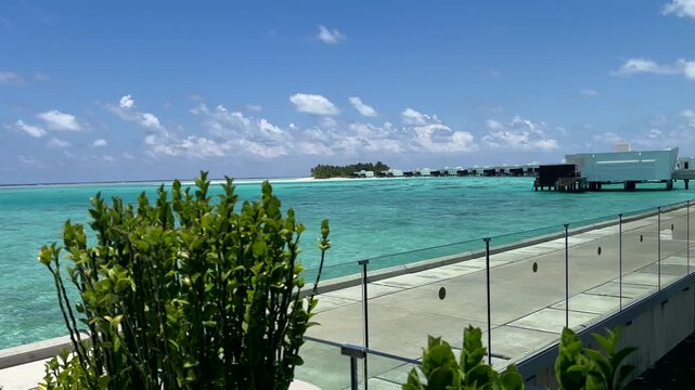 Maldives resort terrace with glass railing green plants overwater bungalows and turquoise ocean view