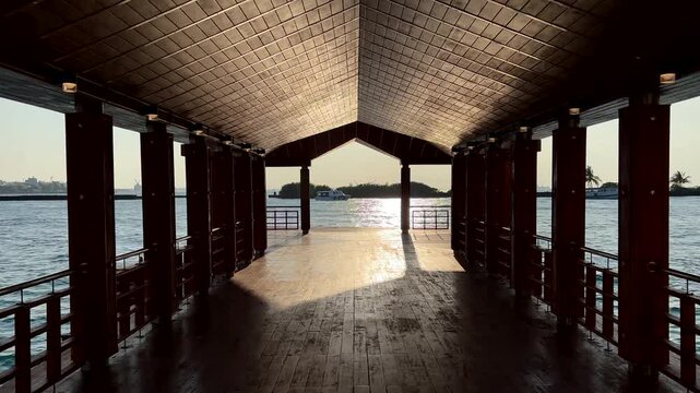 Covered wooden pier with columns leading to ocean view with sunlight reflection Maldives