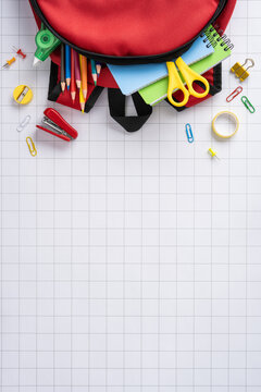 Back to school vertical red backpack with supplies and stationery on grid paper flat lay
