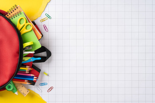 Back to school concept with red backpack full of colorful pencils, notebooks and supplies on graph paper
