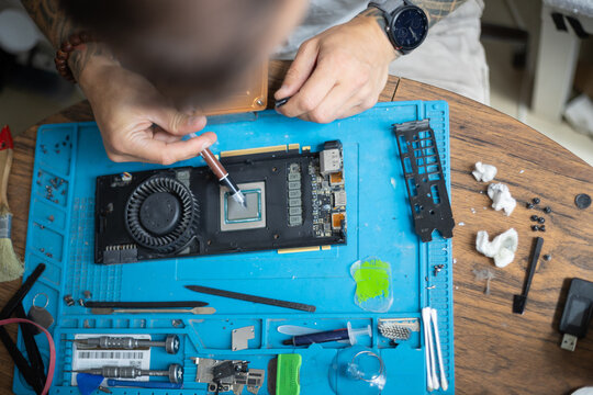 Repair of a graphics card takes place on a wooden table with various tools used for the task in a home workspace during the daytime
