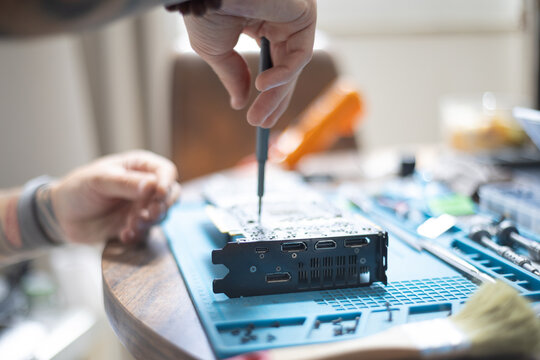 Person working on a computer part on a table with tools and materials in a room during daylight hours