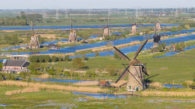 Aerial view of the historic Kinderdijk windmills standing along blue canals surrounded by lush green fields and reeds Kinderdijk, South Holland, Netherlands.