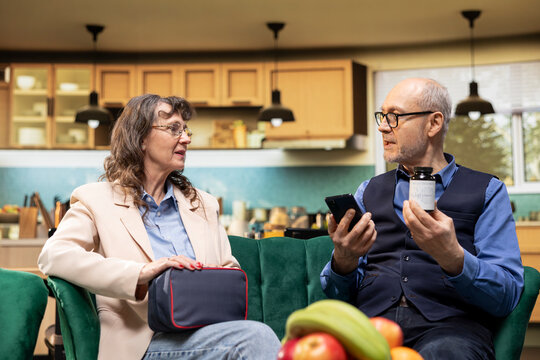 Aged people reading pills box label and online information in living room, prescribed medicine and supplements for in-home routine. Personal care for longevity and healthcare support, recovery.