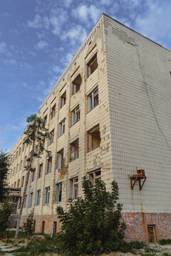 Abandoned multi story building heavily damaged during military conflict with broken windows and shattered facade under blue sky