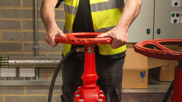 Engineer checking water supply pump on red valve for sprinkler fire protection system. Close up of engineers hands working on a sprinkler fire suppression system. Industrial fire prevention equipment.