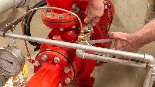 Sprinkler engineer replacing a valve on a red pump set using spanners during maintenance of an industrial fire protection system.