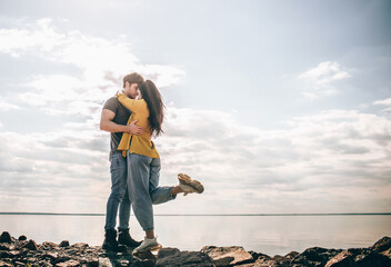 Love and travel. A couple stands against the backdrop of the bay. A man and a woman are standing near a river or sea on stones and hugging. © Vlad