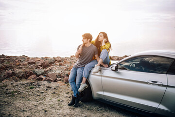 Fototapeta premium young couple by a sports car parked on the beach. Romance and love in a car trip