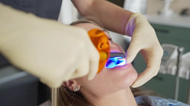 Female dentist performing dental procedure with curing light on patient in clinic. Concept of oral care and medical treatment.