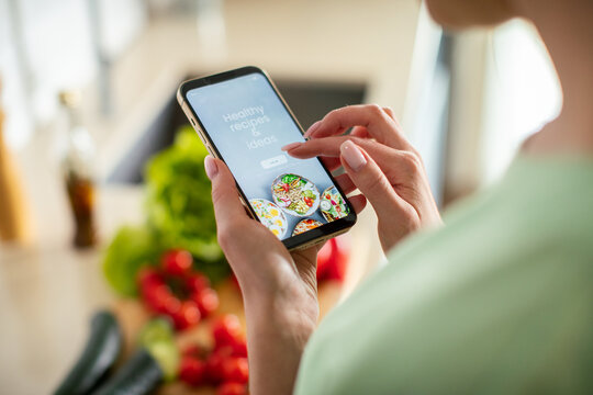Woman using smartphone recipe app in kitchen