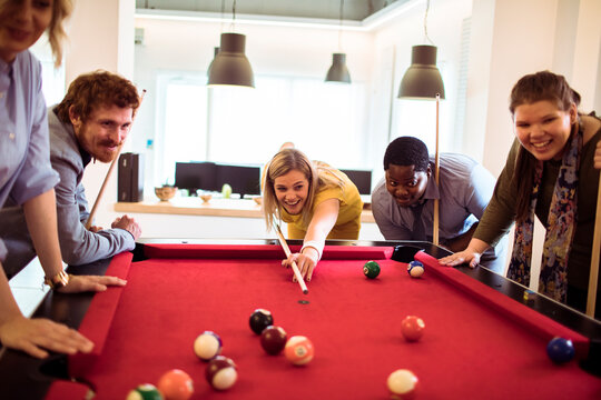 Coworkers playing pool in modern office break room