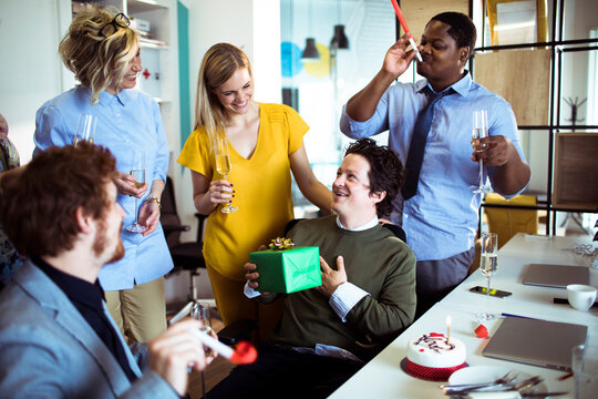 Coworkers celebrating a birthday with gifts and champagne in a modern office