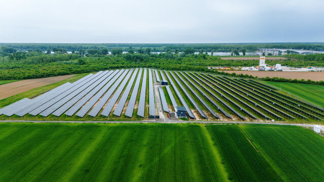 Aerial view of a large solar farm with rows of photovoltaic panels surrounded by lush green agricultural fields and dense forests near a river Sabac, Vojvodina, Serbia.