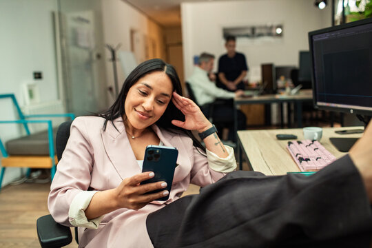 Young businesswoman relaxing with smartphone in modern office