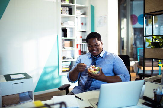 Smiling businessman eating salad at office desk