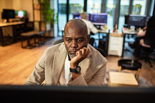 Pensive middle-aged businessman working at computer in modern office