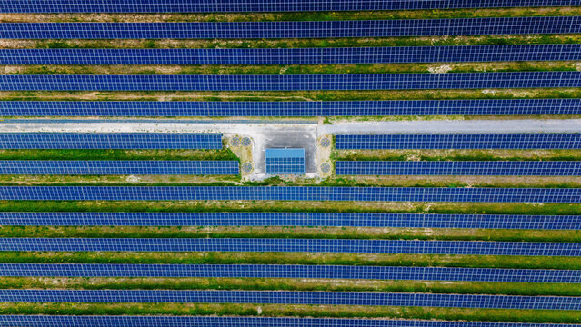 Aerial view of rows of blue solar panels in a large photovoltaic farm with a central utility building Sabac, Vojvodina, Serbia.