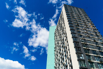 Fototapeta premium Low angle view of modern high rise apartment building tower with stylish facade against vibrant blue sky with fluffy white clouds