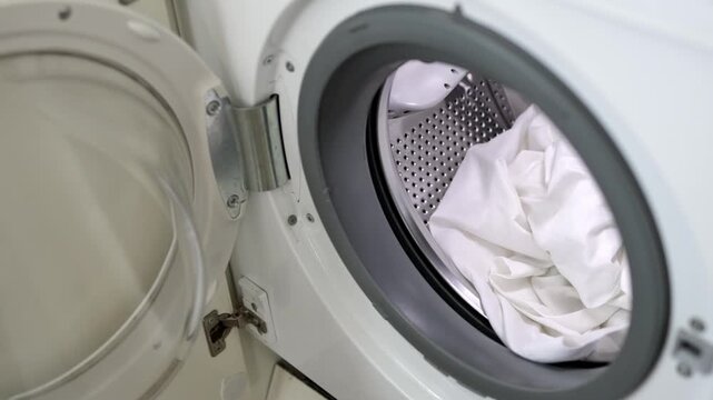 White laundry being loaded into a washing machine, showcasing the door opening and the interior drum filled with freshly washed clothes in a domestic setting