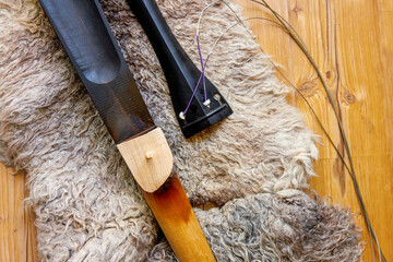 Broken contrabass neck joint with fingerboard and tailpiece on felted wool locks rug. Close up © Dina