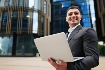 Fototapeta premium Smiling professional enjoys working on laptop in vibrant urban setting during sunny day