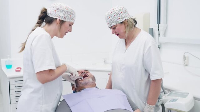 Professional female dentist and her assistant performing a tooth extraction on a male patient in a modern, bright dental clinic